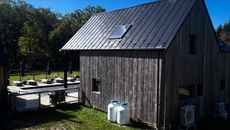 Rustic wooden building with a dark metal roof, solar panel, and propane tanks on a sunny day.