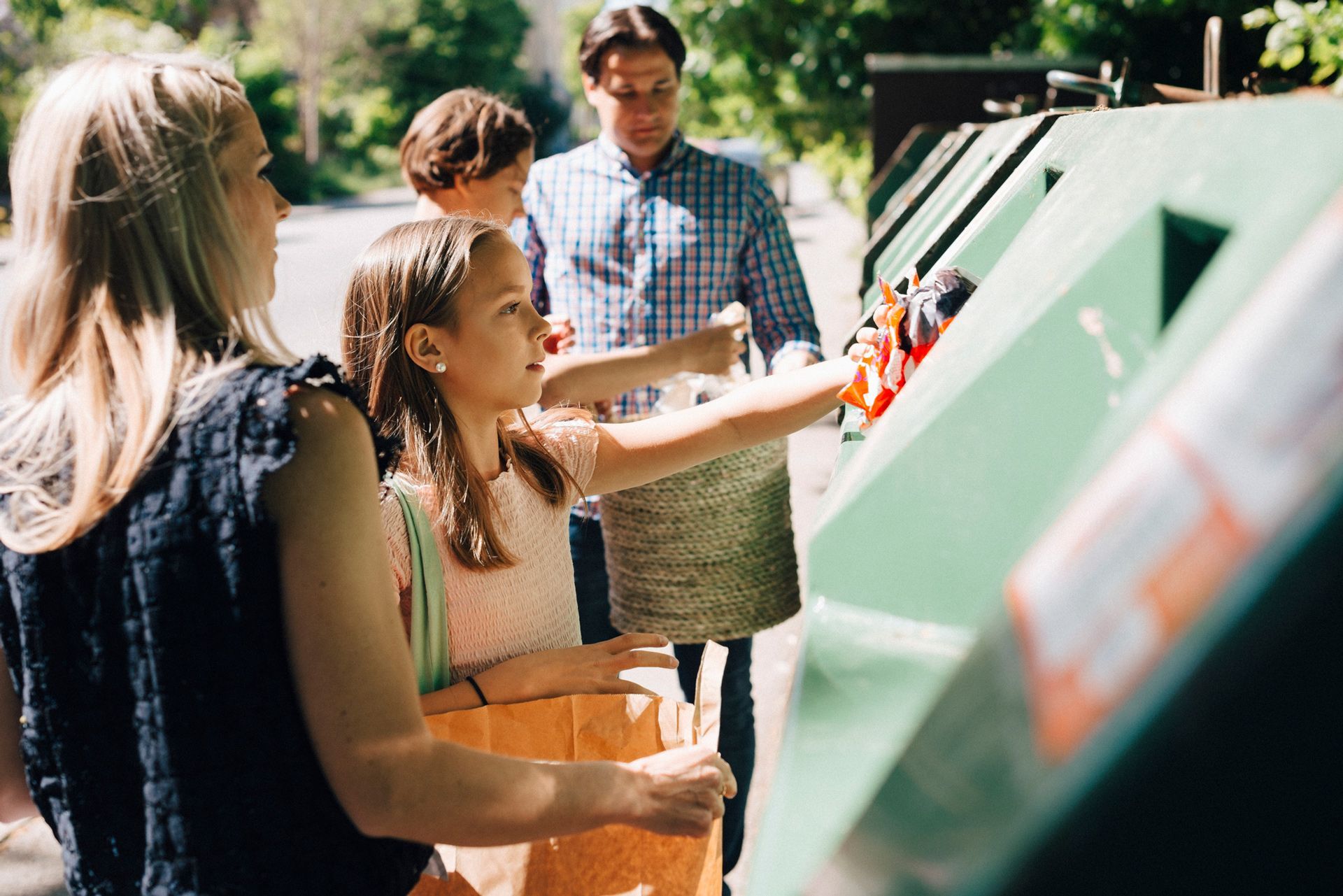 A family is putting their trash in a recycling bin.