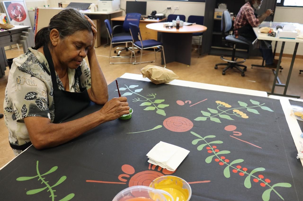 Woman painting floral design on black fabric in a studio.