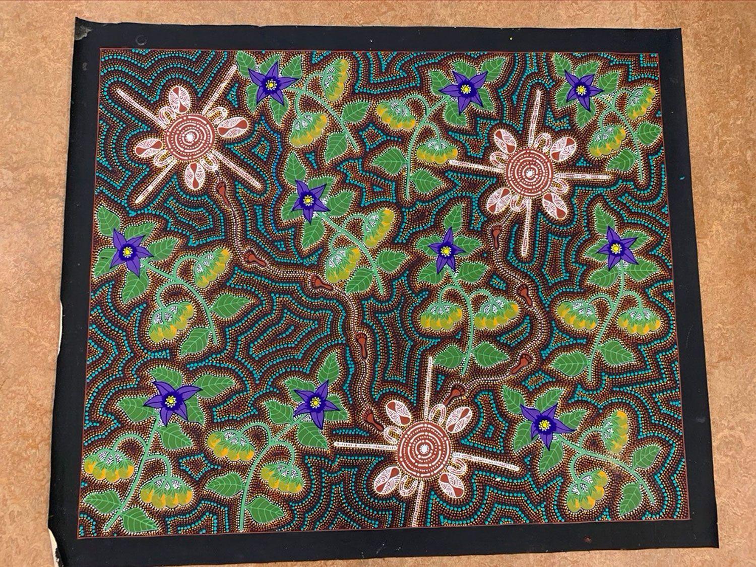 Beaded artwork of a flowering vine with green leaves, brown branches, and pink and blue flowers on a dark background.
