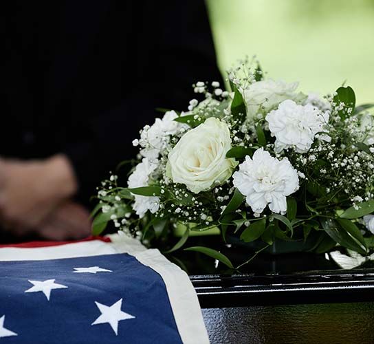 A United States flag draped over a casket with a white floral arrangement placed on top.