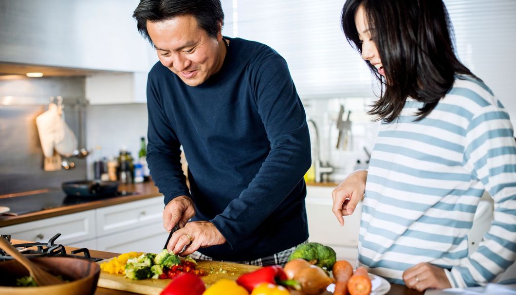 A man and a woman are cutting vegetables on a cutting board in a kitchen.