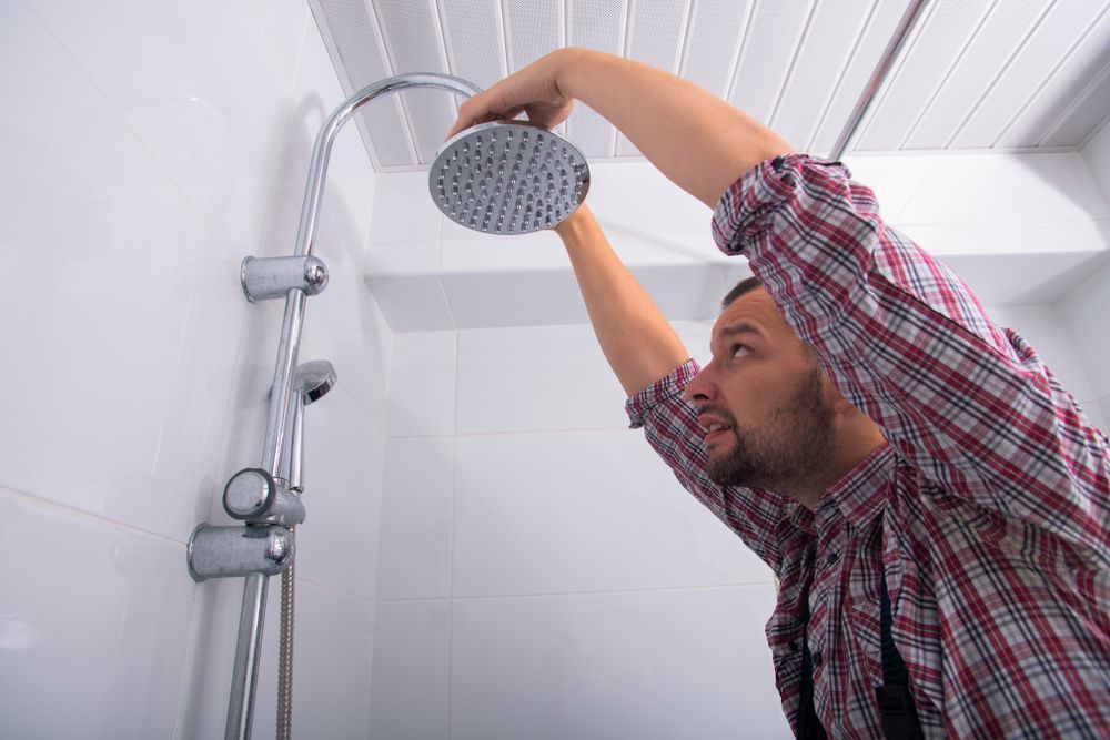 A Man is Fixing a Shower Head in a Bathroom — Home Nursing Services In Laurieton, NSW