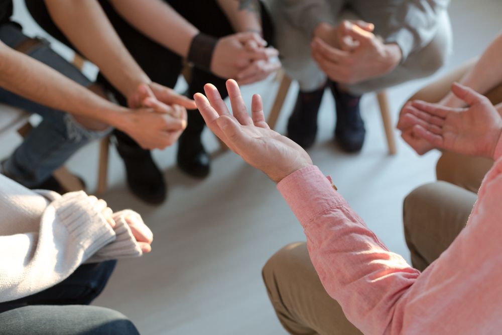 A Group of People Are Sitting in a Circle Holding Hands — Home Nursing Services In Macquarie, NSW