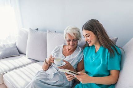 A Nurse is Sitting Next to an Elderly Woman on a Couch — Home Nursing Services In Macquarie, NSW
