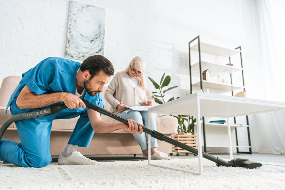 A Man Is Cleaning The Floor With A Vacuum Cleaner — Home Nursing Services In Williamtown, NSW