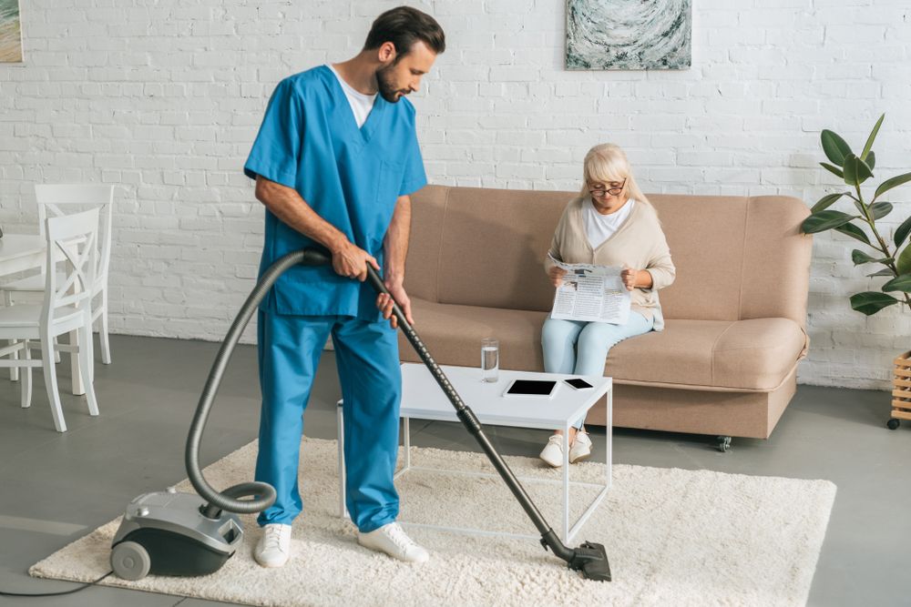 A Man Is Vacuuming The Floor In A Living Room — Home Nursing Services In Fennell Bay, NSW