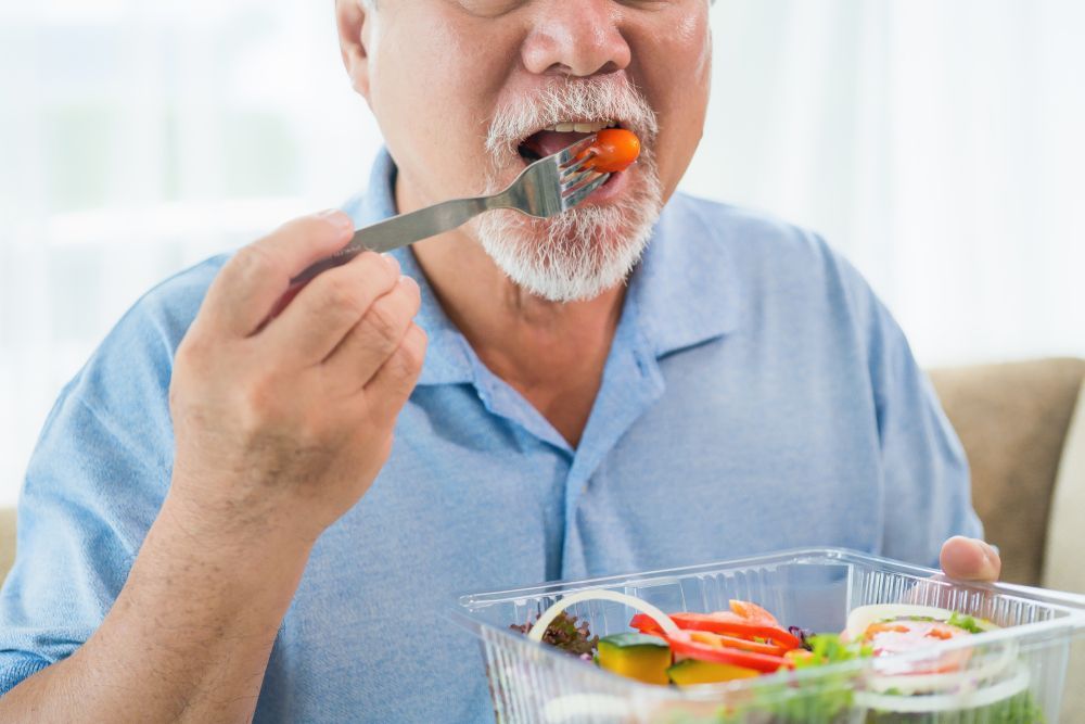 An Elderly Man Is Eating A Salad With A Fork — Home Nursing Services In Toronto, NSW