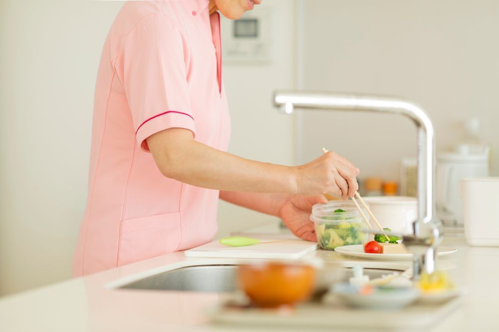 A Woman in a Pink Uniform is Preparing Food in a Kitchen — Home Nursing Services In Macquarie, NSW