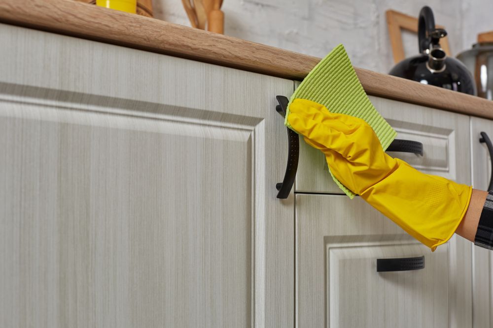 A Person Wearing Yellow Gloves is Cleaning a Kitchen Cabinet With a Cloth — Home Nursing Services In Port Macquarie, NSW