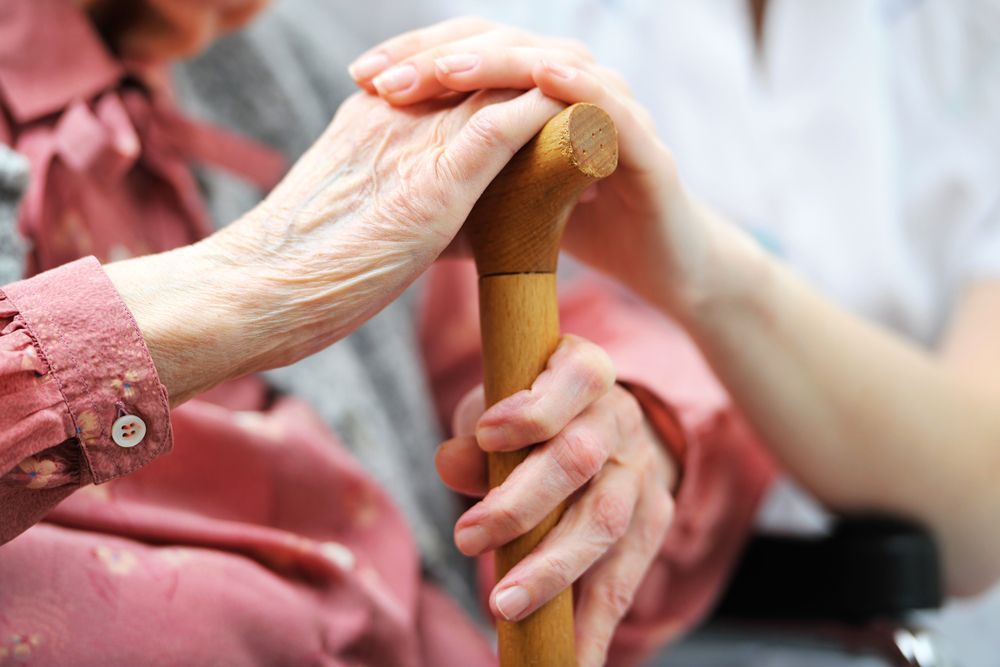 Hands Holding a Wooden Cane, With Another Hand Gently Resting on Top — Home Nursing Services in Parramatta, NSW