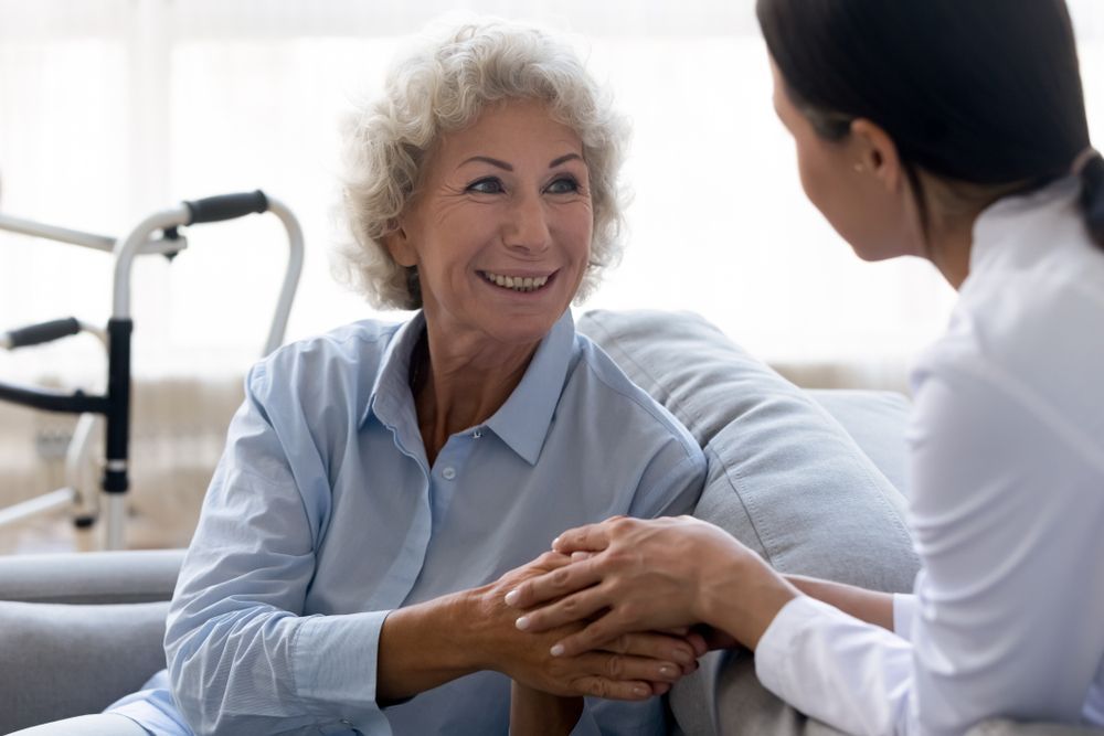 An elderly woman is sitting on a couch holding the hand of a nurse. — Home Nursing Services In Port Macquarie, NSW