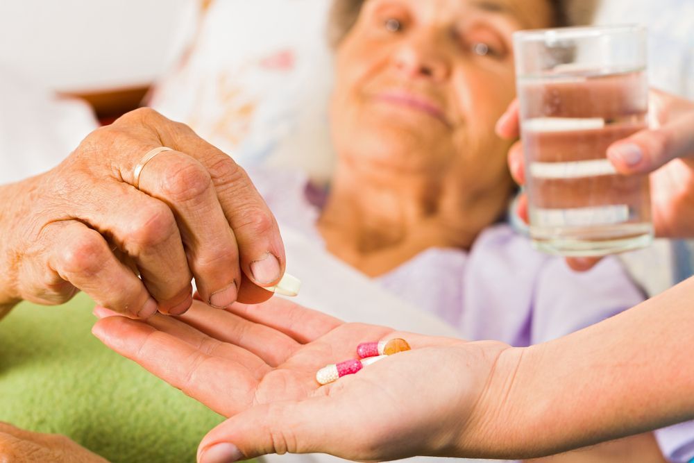 A Person Is Giving An Elderly Woman A Pill And A Glass Of Water — Home Nursing Services In Toronto, NSW
