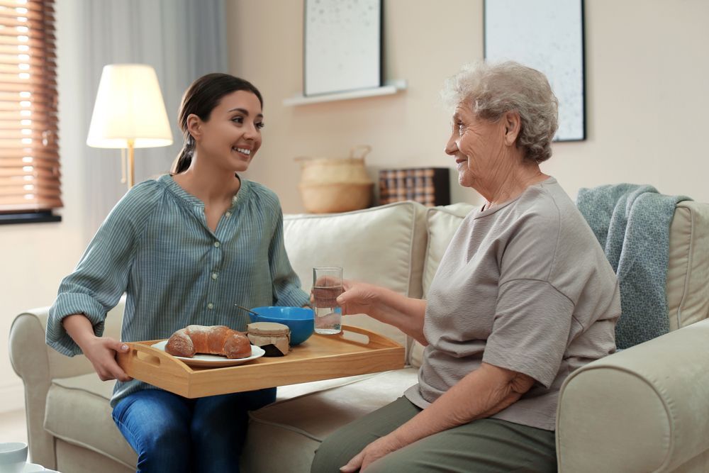 A Woman Is Sitting On A Couch Holding A Tray Of Food — Home Nursing Services In Kew, NSW