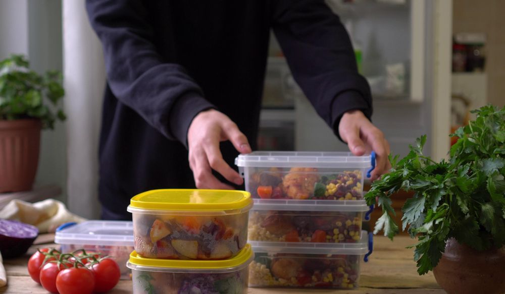 A Man Is Putting Food In Plastic Containers On A Table — Home Nursing Services In Medowie, NSW