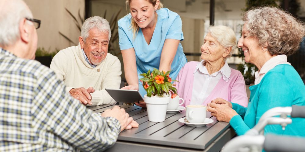 A Group Of Elderly People Are Sitting At A Table With A Nurse — Home Nursing Services In Medowie, NSW