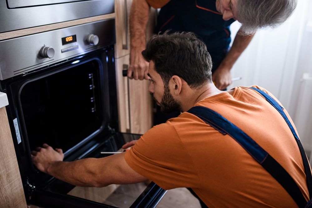 Two Men Are Working On An Oven In A Kitchen — Home Nursing Services In Lake Cathie, NSW