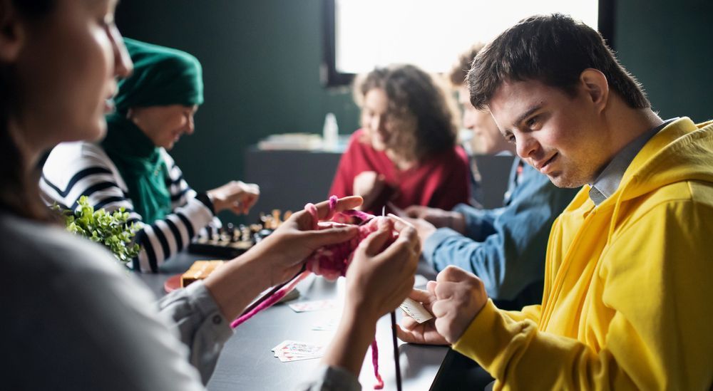 A Group of People Are Sitting Around a Table Knitting — Home Nursing Services In Port Macquarie, NSW