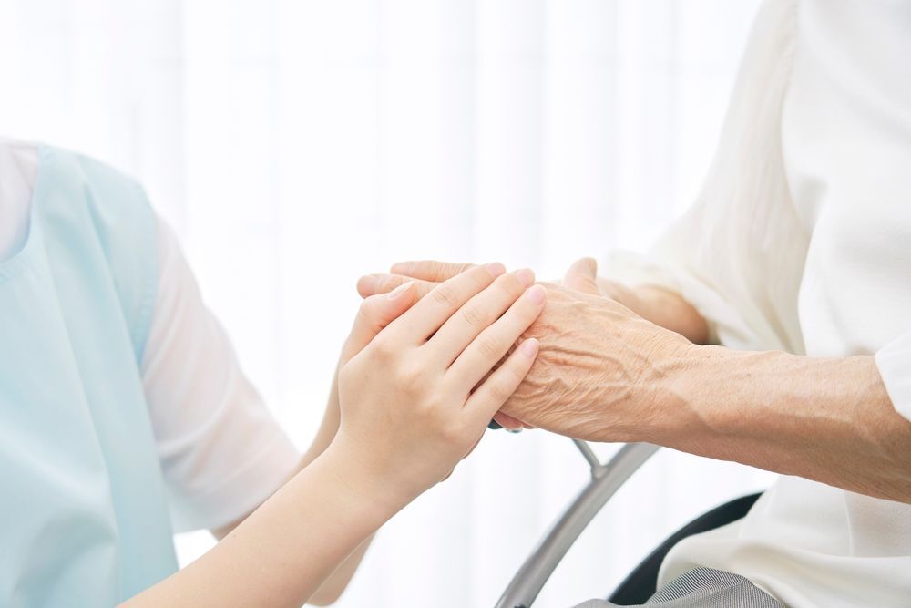 A Woman Is Holding The Hand Of An Elderly Woman In A Wheelchair — Home Nursing Services In Dora Creek, NSW