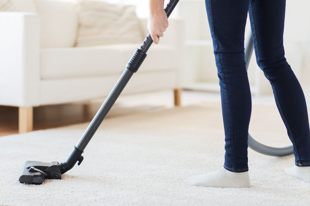 A Woman Is Vacuuming The Carpet In A Living Room — Home Nursing Services In Newcastle, NSW