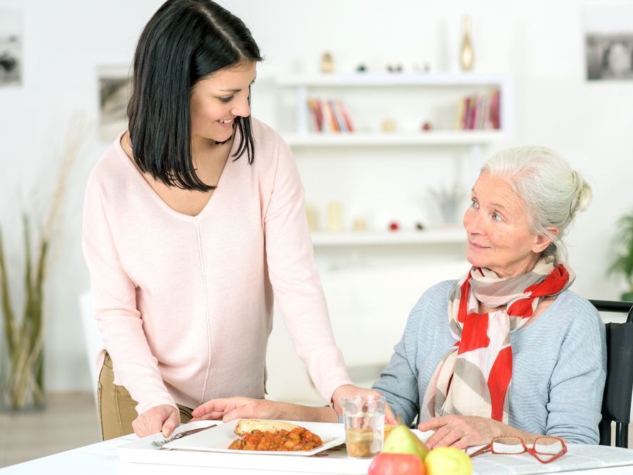 A Woman in a Wheelchair is Sitting at a Table With a Man — Home Nursing Services In Port Macquarie, NSW