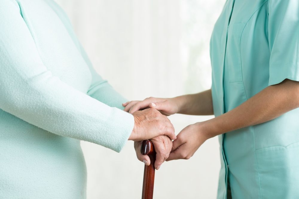 A Nurse Is Holding The Hand Of An Elderly Woman Holding A Cane — Home Nursing Services In Warners Bay, NSW