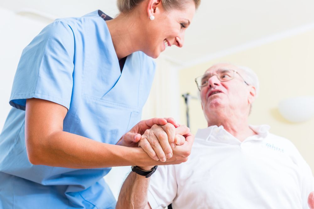 A Nurse Is Holding The Hand Of An Elderly Man — Home Nursing Services In Warners Bay, NSW