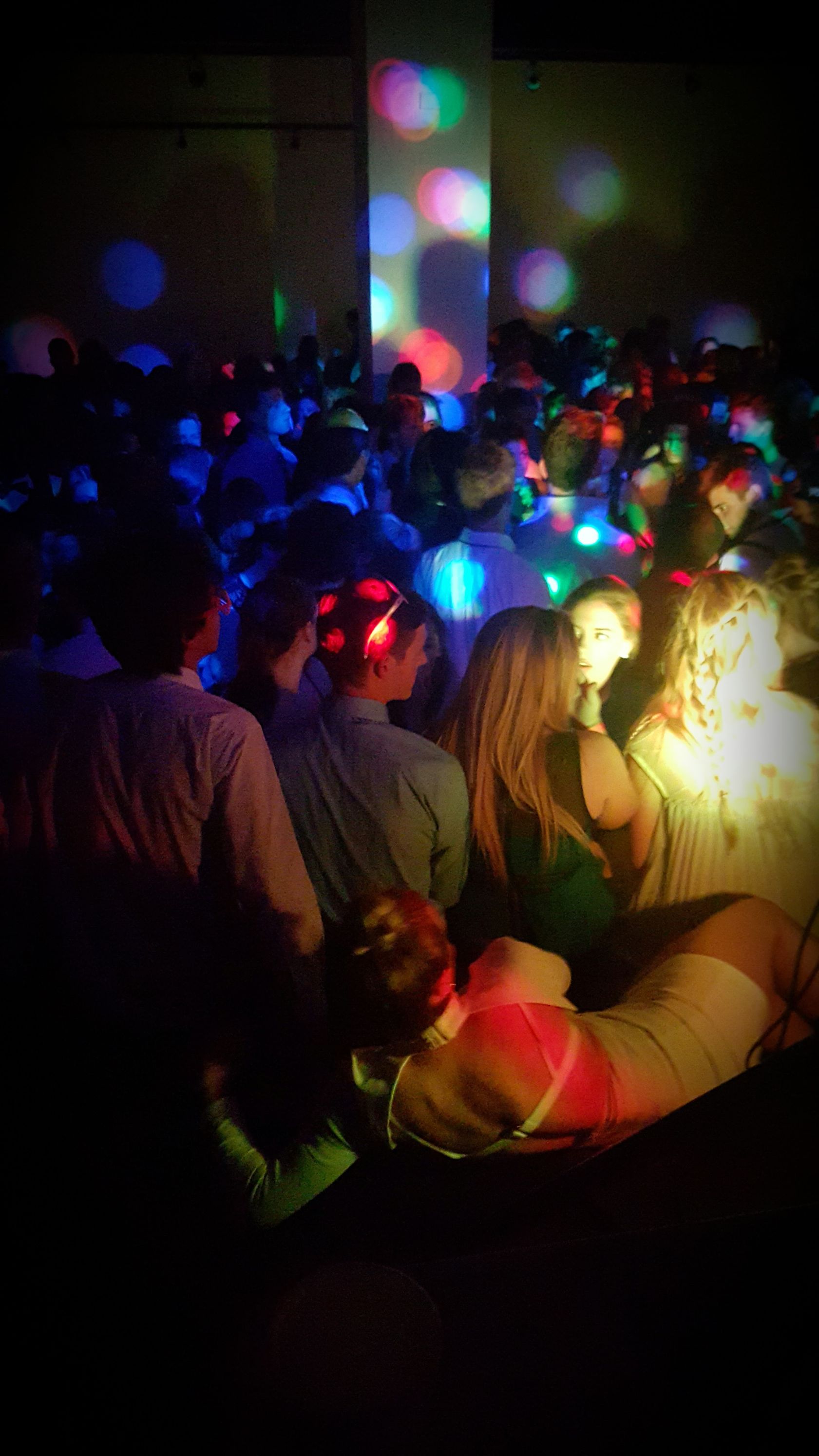 A crowd of people are sitting in a dark room wearing headphones.