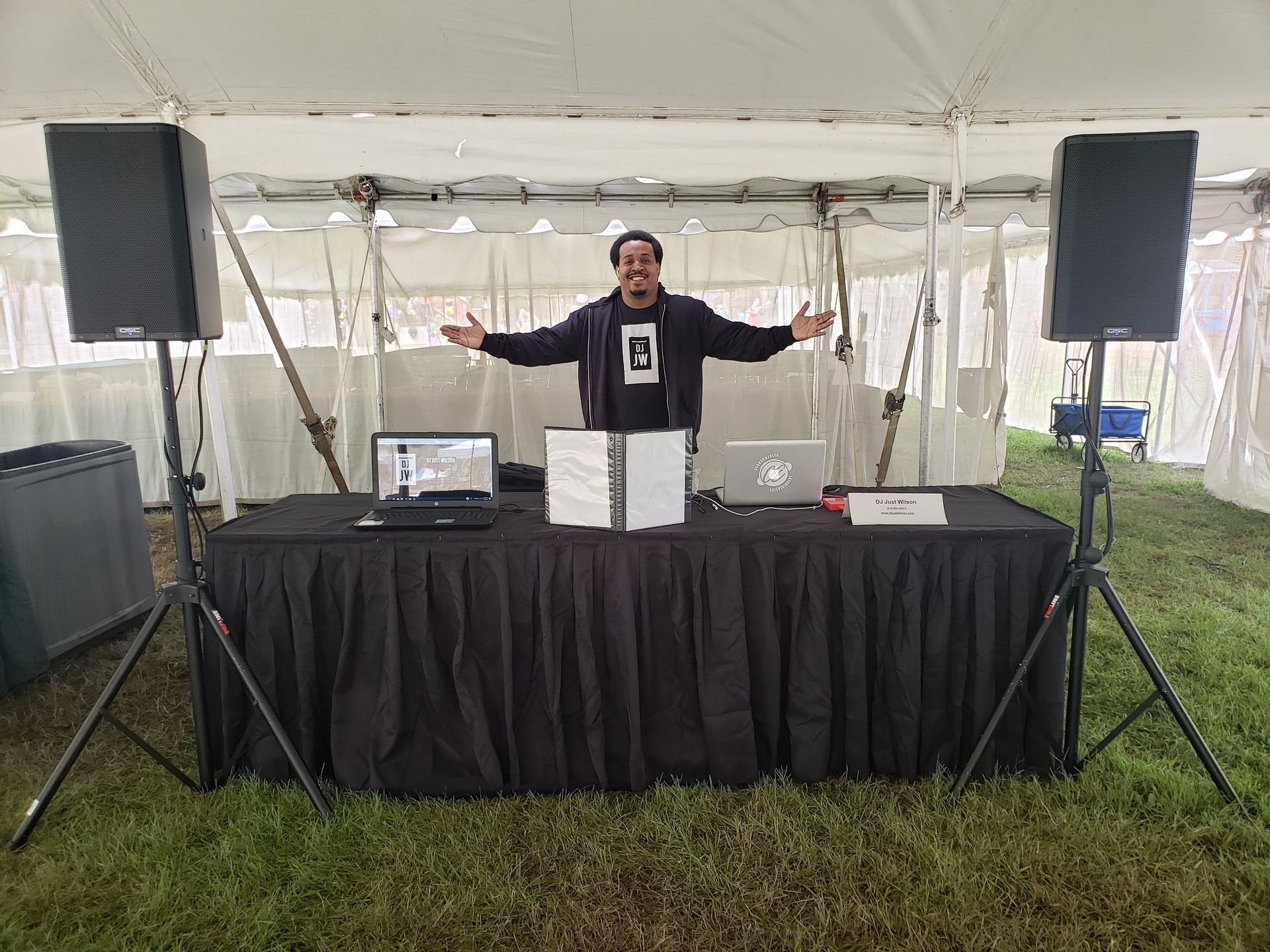 A man is standing in front of a dj booth under a tent.