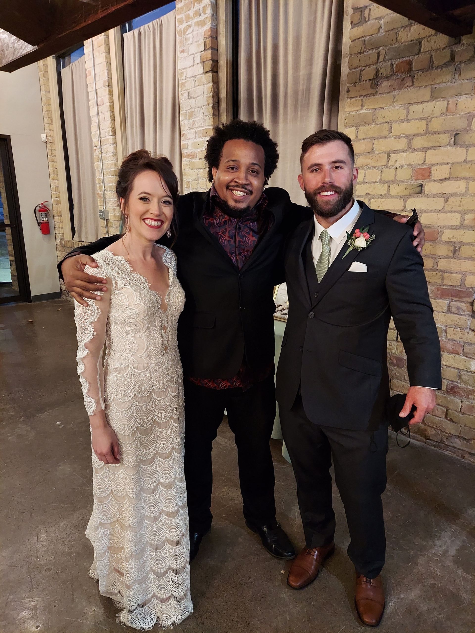 A bride and groom are posing for a picture with a man in a suit.
