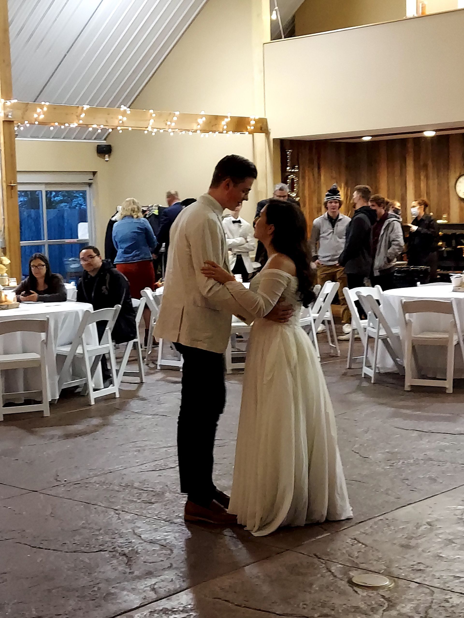 A bride and groom are dancing in a room with tables and chairs.