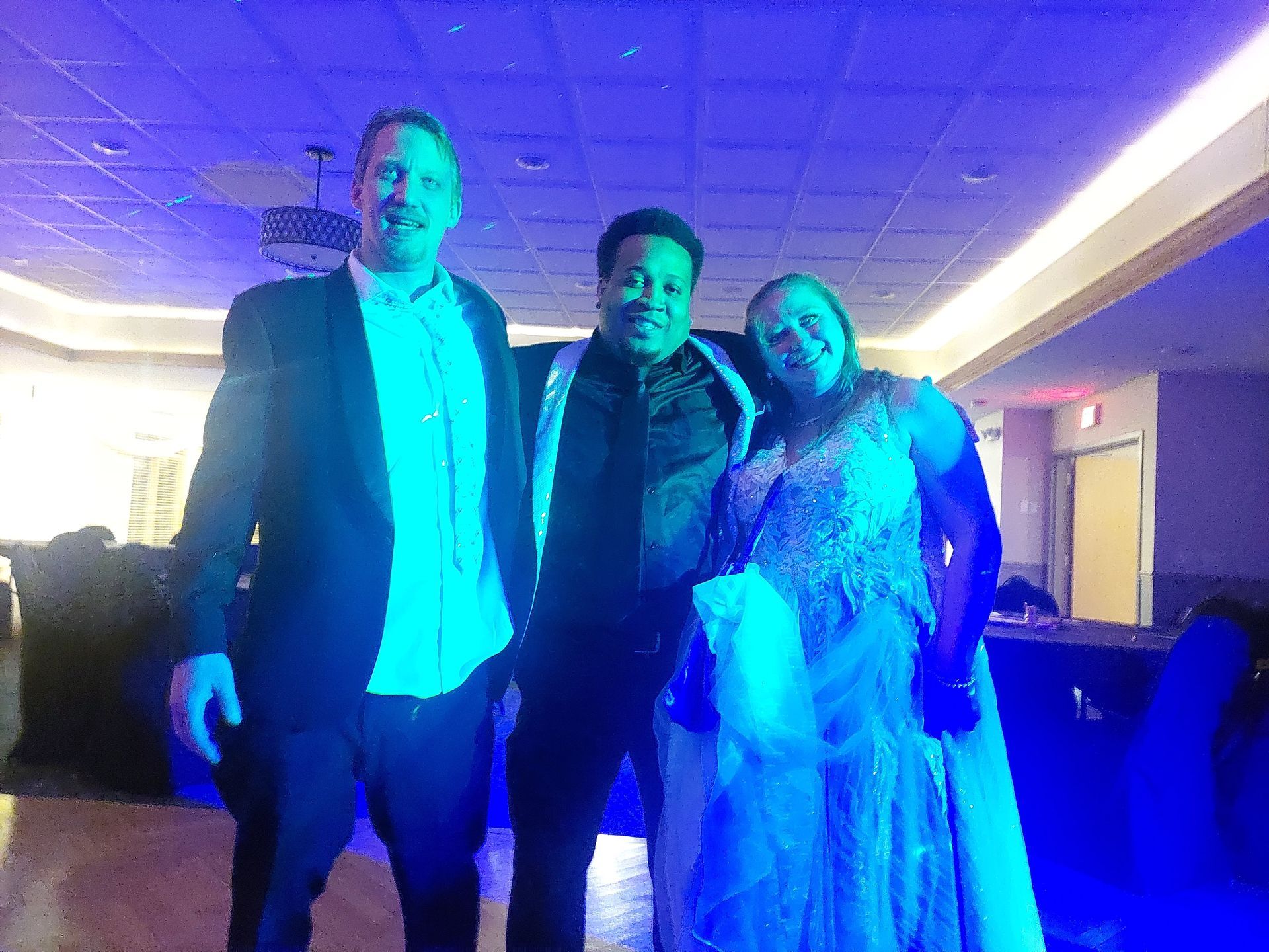 Three people are posing for a picture in a room with blue lights.