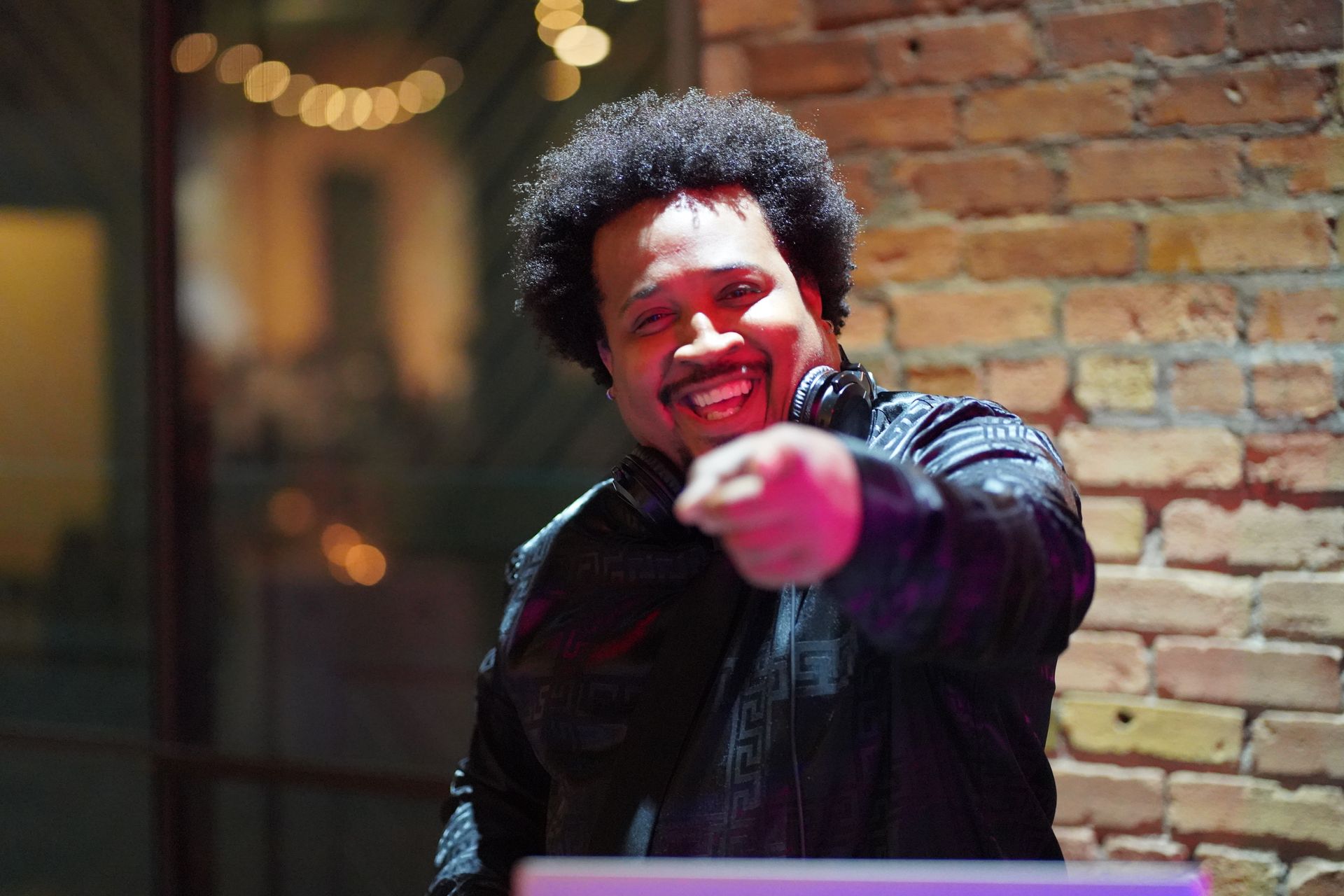 A man with curly hair is pointing at the camera while wearing headphones.