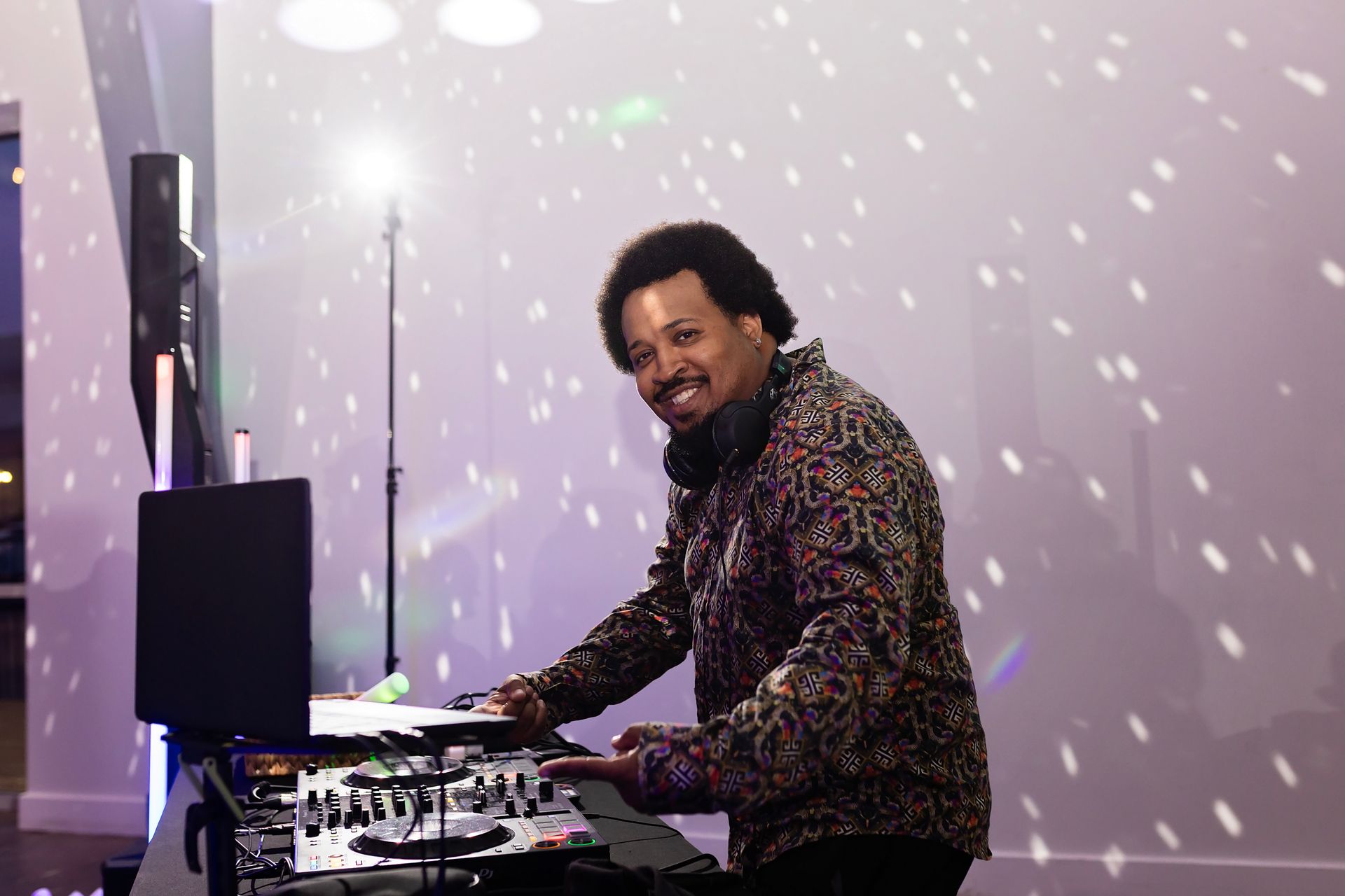 DJ at a turntable under purple stage lighting with a disco-ball pattern on the wall