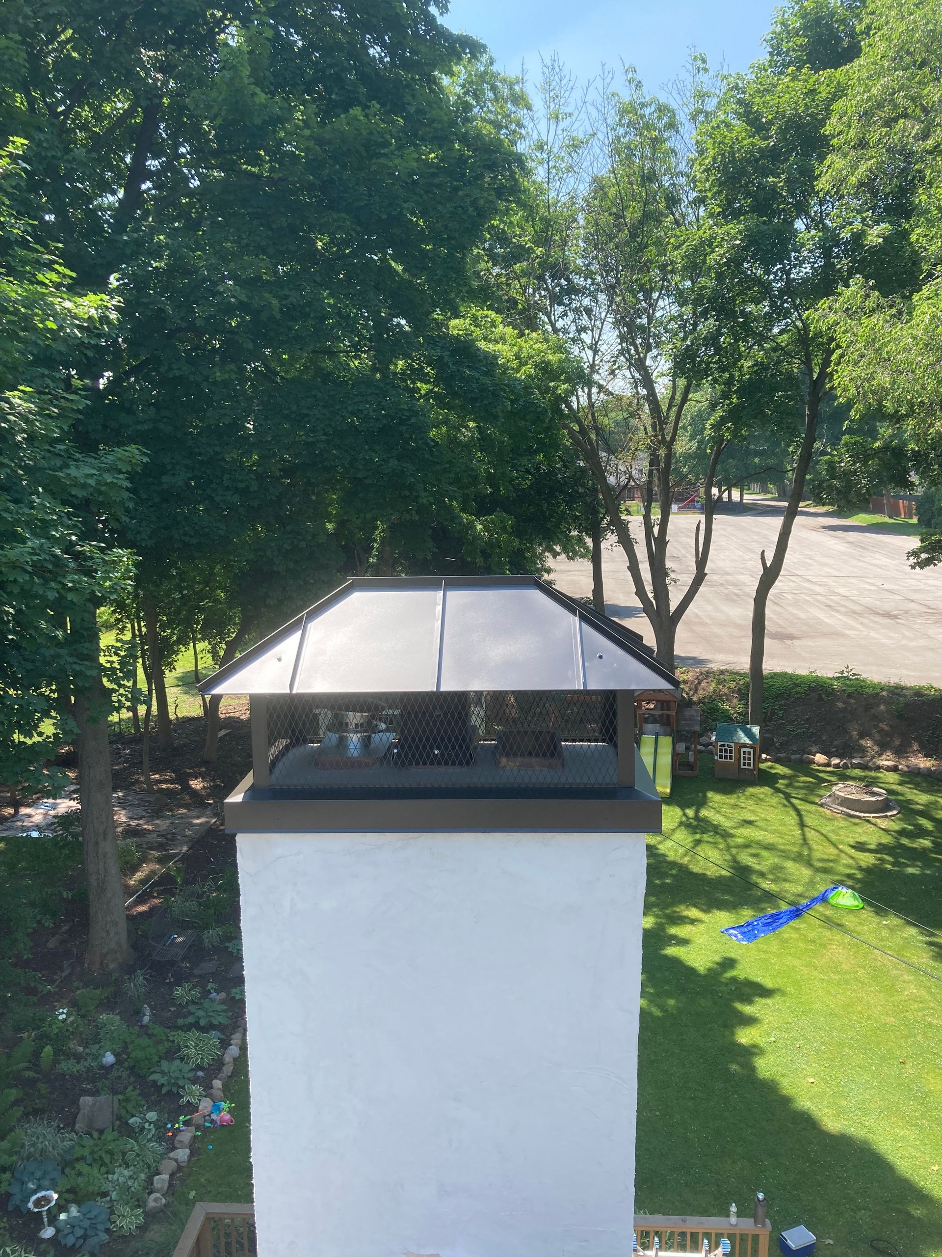 White chimney with a metal cap, in a yard with trees. Sunny day.