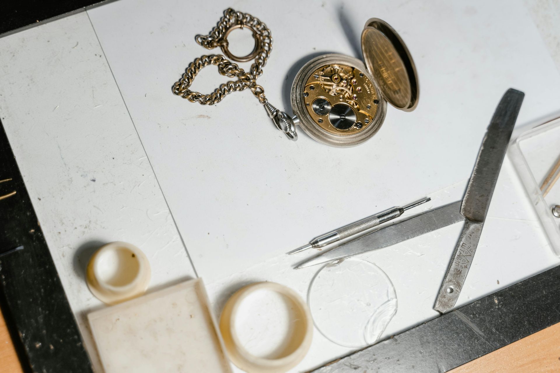 A pocket watch sits on a table next to a pair of scissors