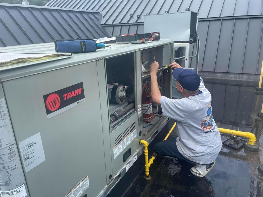 A man is working on an air conditioner on the roof of a building.