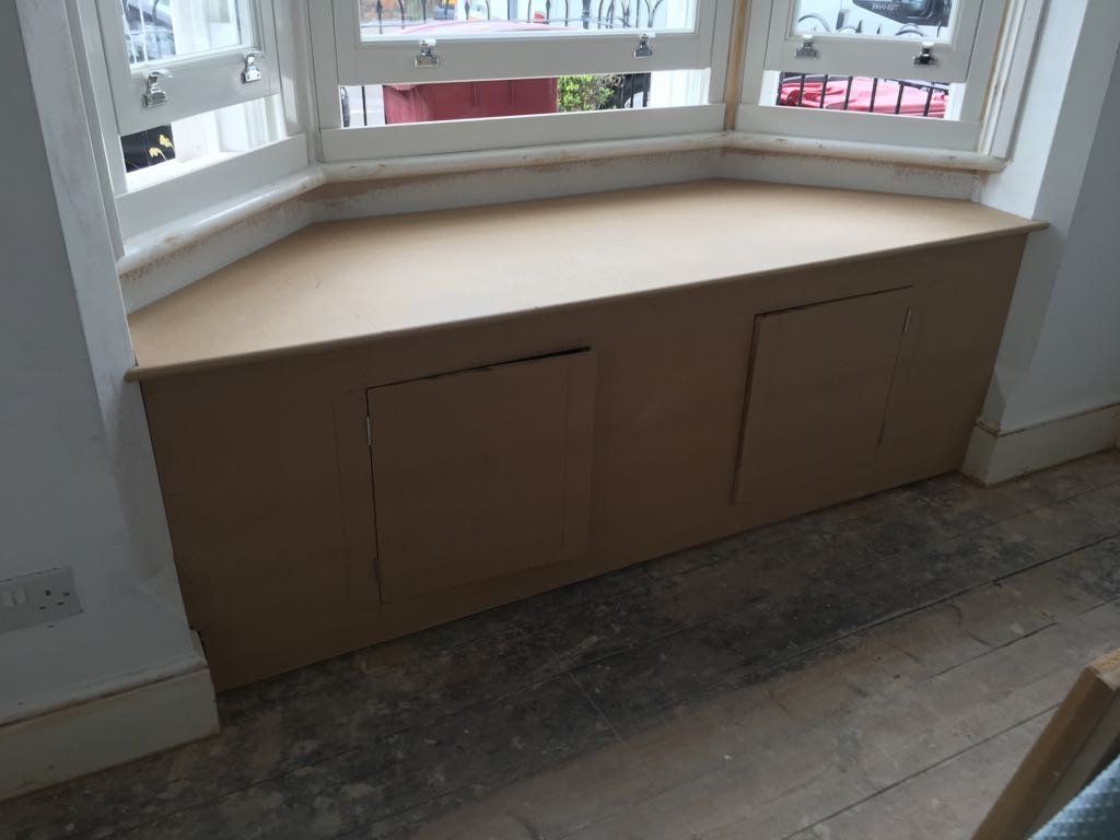 A window seat with a wooden cabinet underneath it.