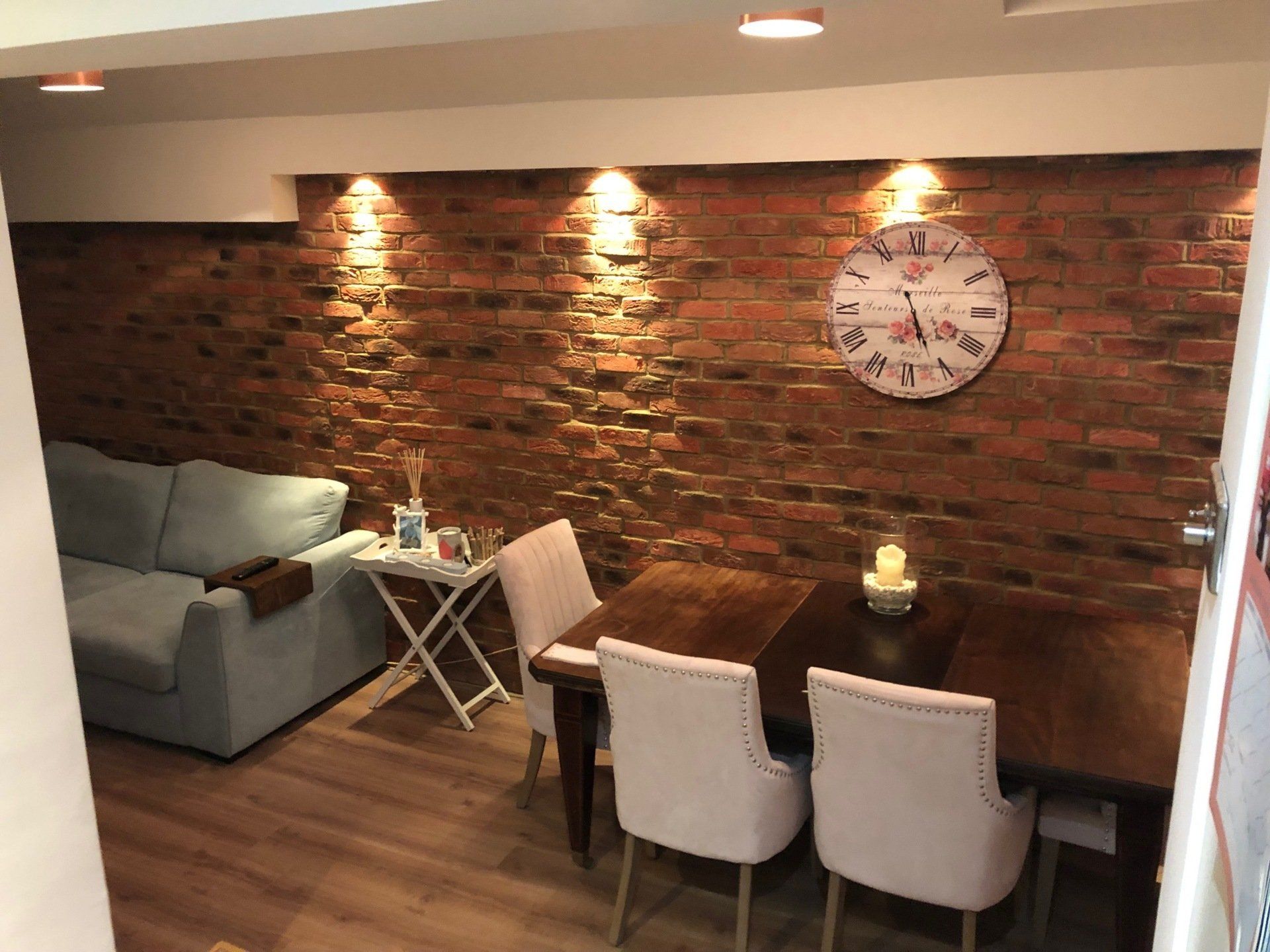 A living room with a brick wall and a clock on the wall.