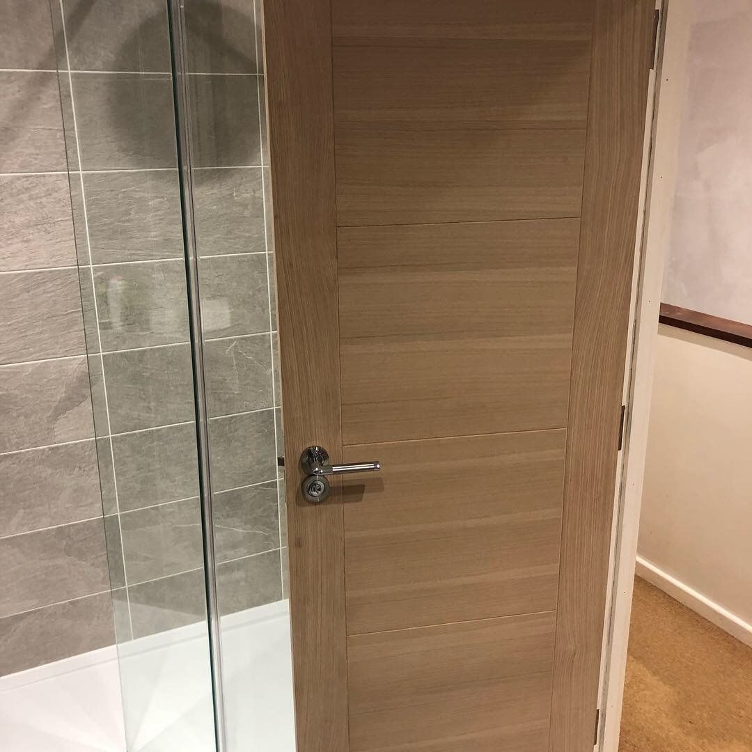 A bathroom with a wooden door and a glass shower door.