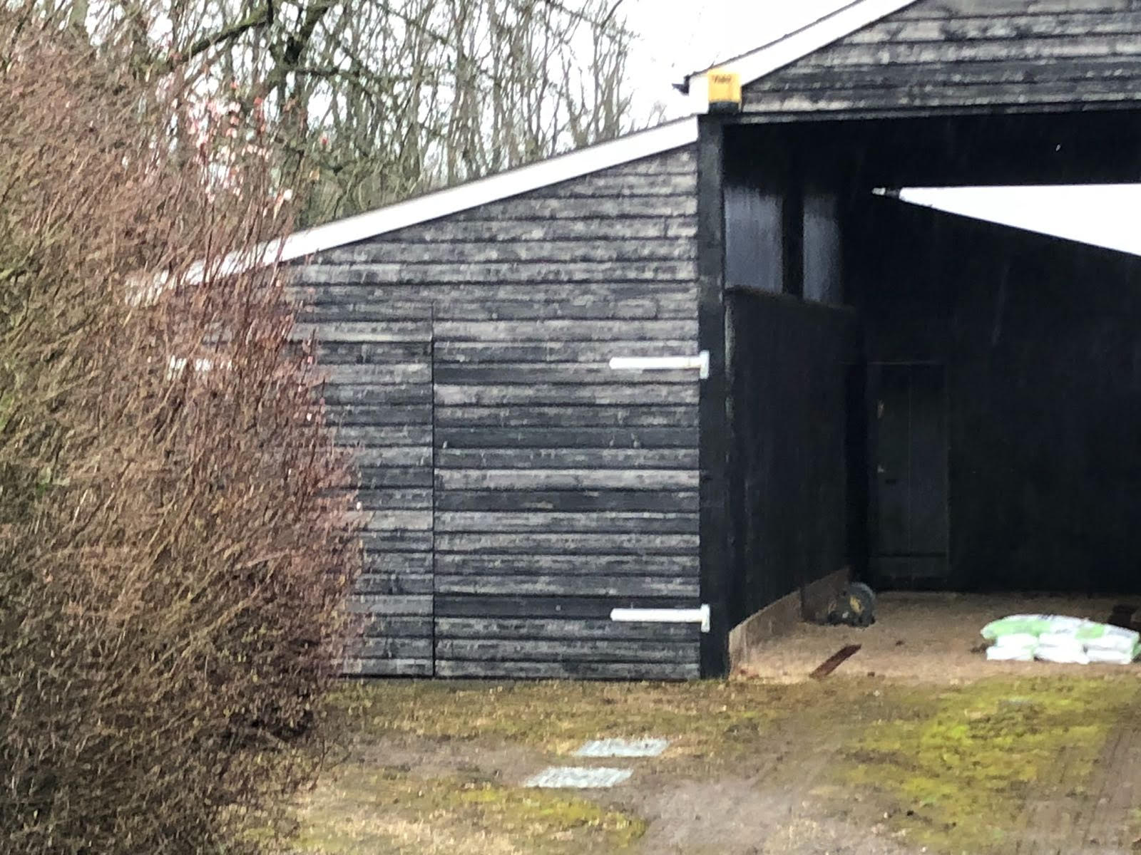 A black garage with a white roof is sitting in the middle of a field.