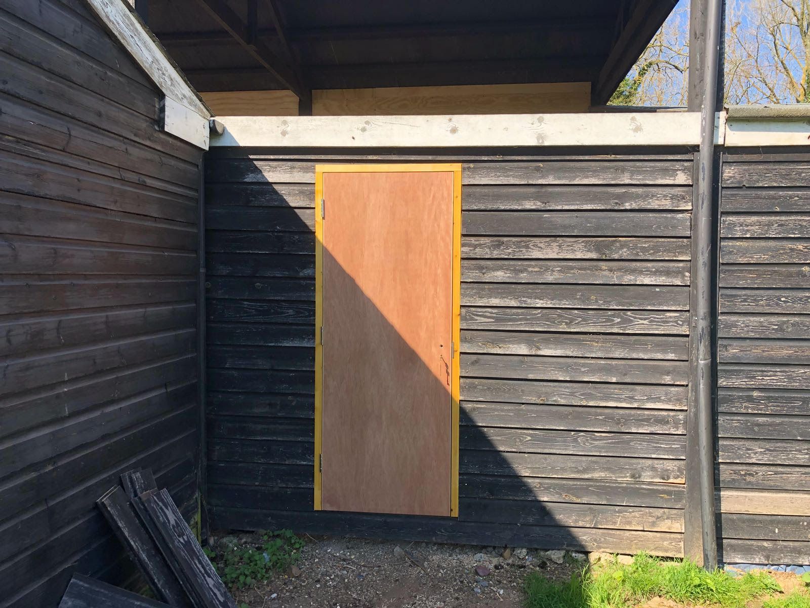 A wooden door is hanging on a black wooden wall.