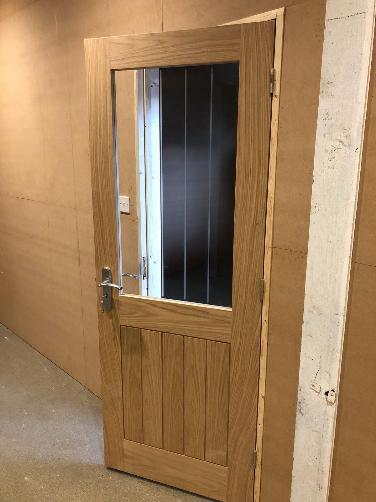A wooden door with a glass window is sitting in a hallway.