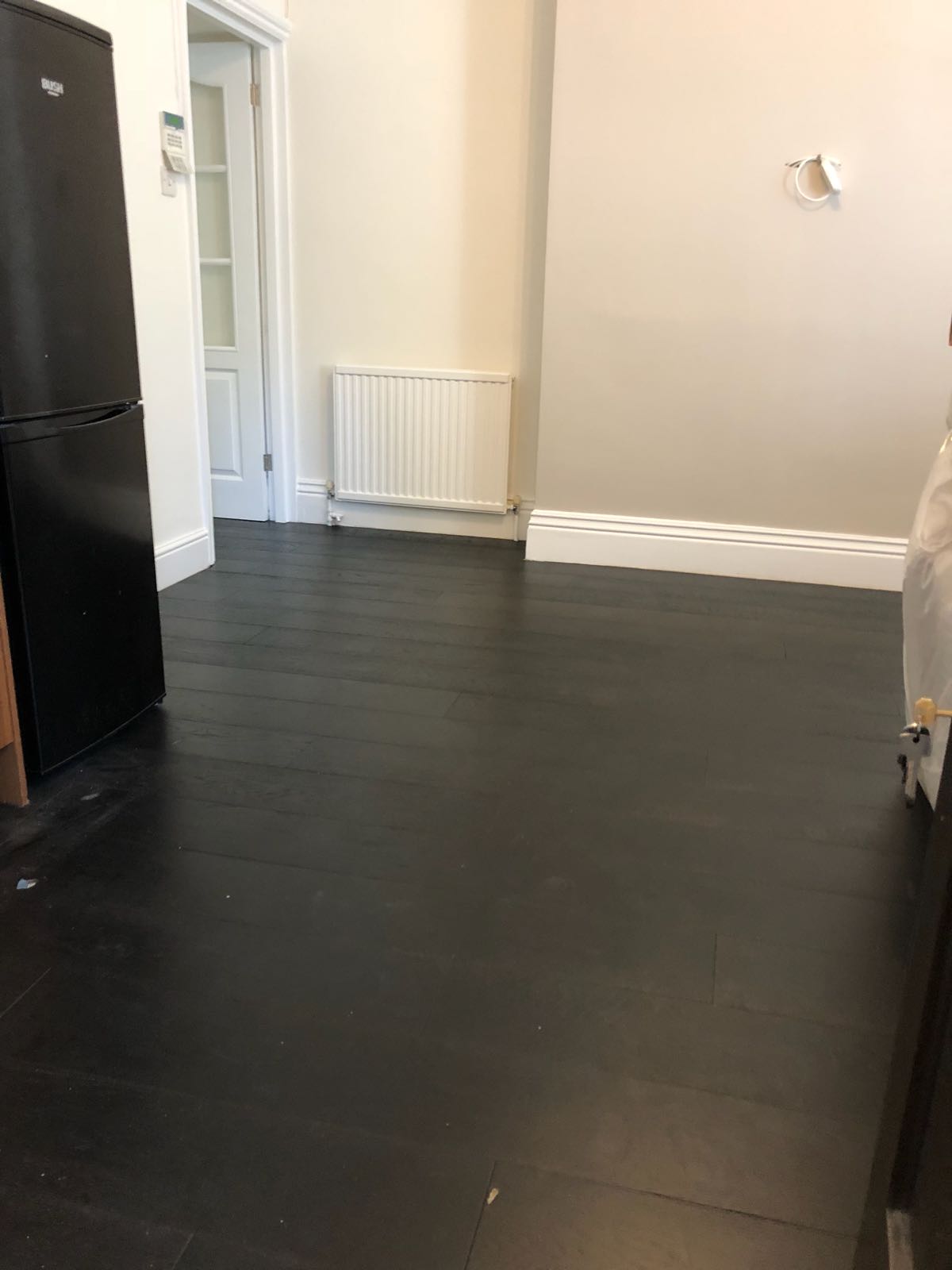A kitchen with a black refrigerator and a black wooden floor.