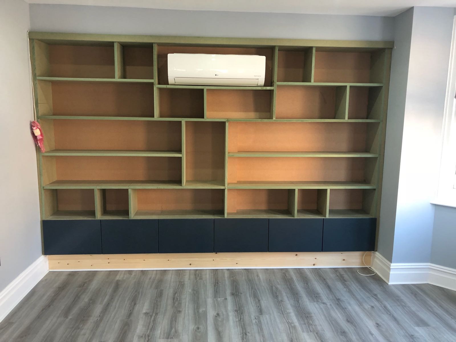 A room with a bookshelf and a air conditioner on top of it.