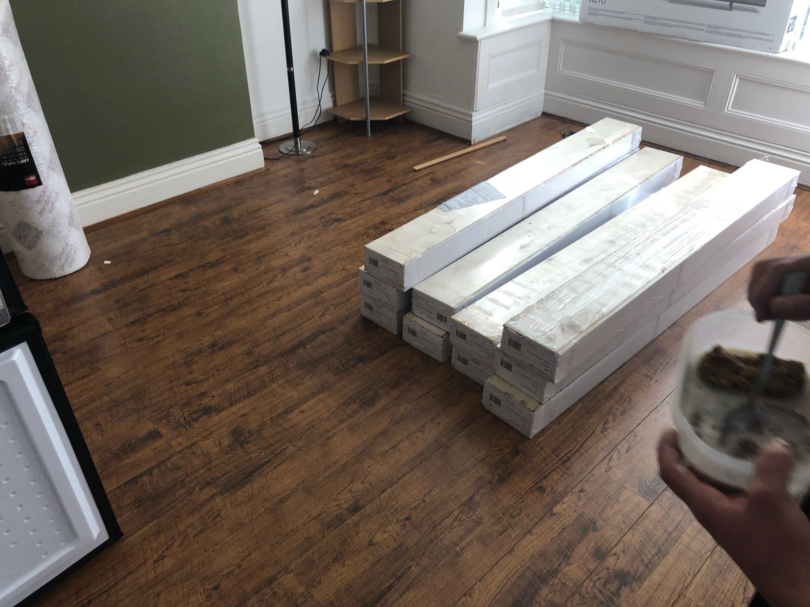 A person is holding a cup of coffee in a living room with wooden floors.