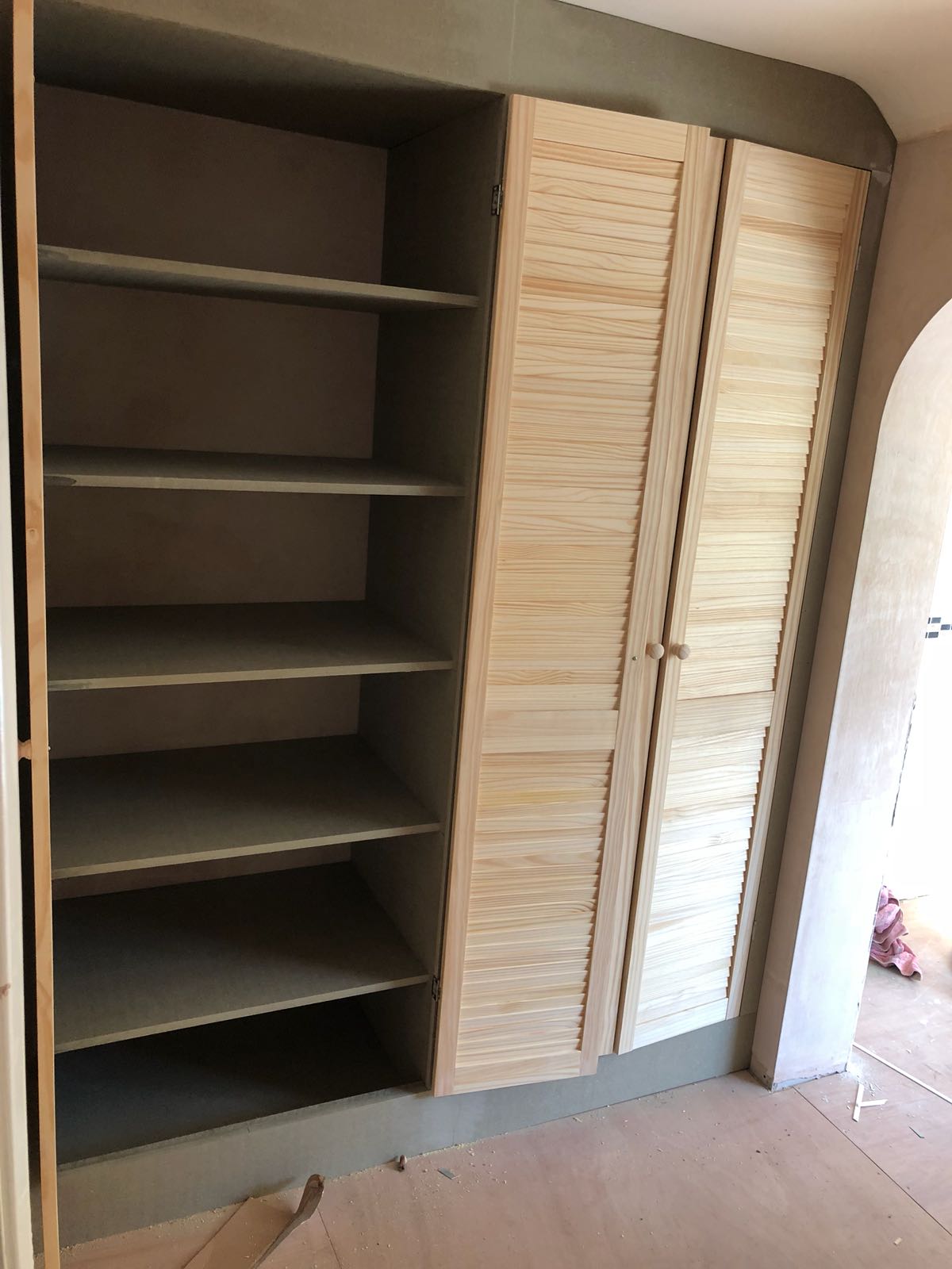 A closet with shutter doors and shelves in a room.