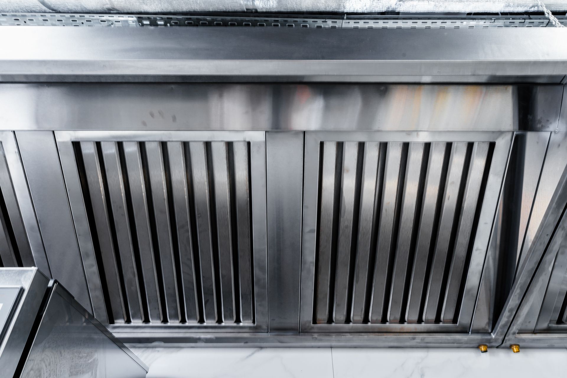A close-up view of stainless steel commercial kitchen hood grease filters mounted above a workspace.