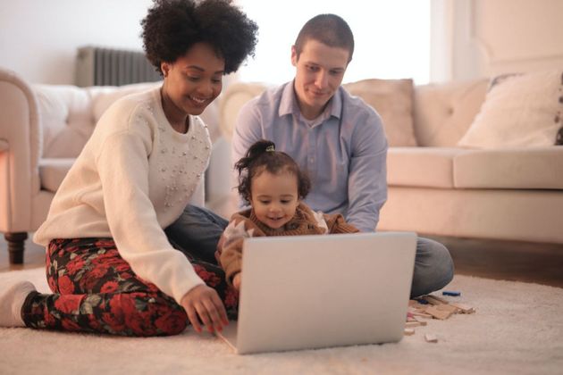 A family is sitting on the floor looking at a laptop computer.