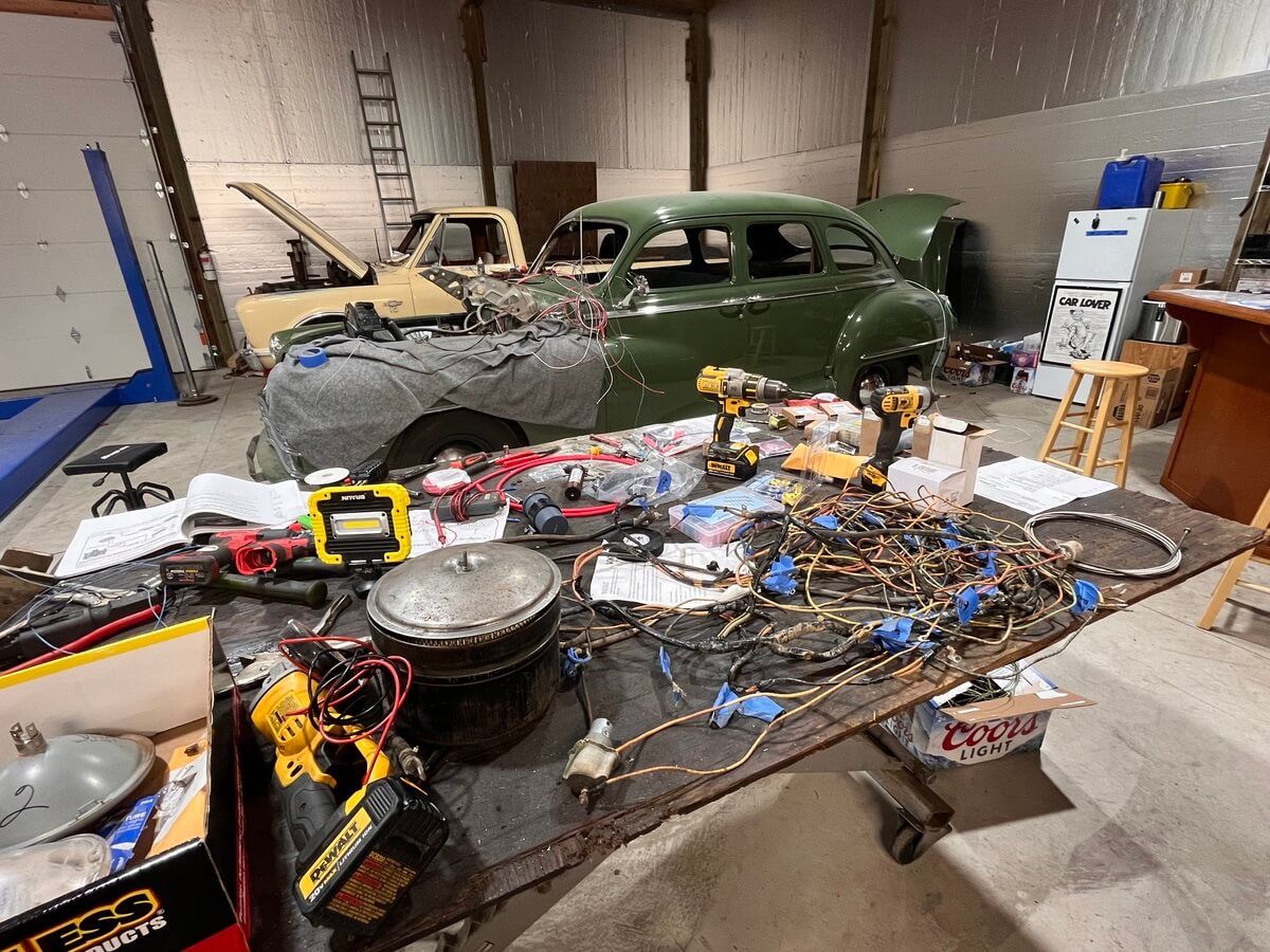 A messy table with tools and a car in the background